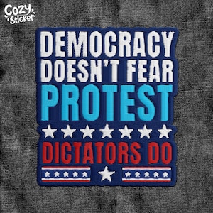 May include: Embroidered patch with the text "DEMOCRACY DOESN'T FEAR PROTEST DICTATORS DO" in white, blue, and red. The patch features stars and stripes design elements, and the Cozy Sticker logo.