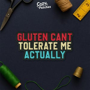 May include: Embroidered patch with the text "GLUTEN CANT TOLERATE ME ACTUALLY" in red, cream, and blue. The patch is surrounded by sewing tools, including scissors, a thimble, and a measuring tape, on a dark blue background. The brand name "Cozy Patches" is in the top right corner.
