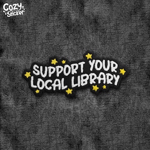 May include: Embroidered patch with the text "SUPPORT YOUR LOCAL LIBRARY" in white on a black background. Yellow star accents surround the text. The patch is on a dark grey denim fabric. The top left corner has the text "Cozy Sticker".