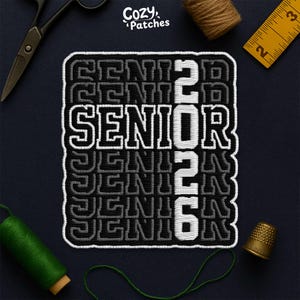 May include: Embroidered patch with the word "SENIOR" and the number "2026" in white and gray. The patch is rectangular with a white border. The patch is surrounded by sewing tools, including scissors, thread, and a thimble.