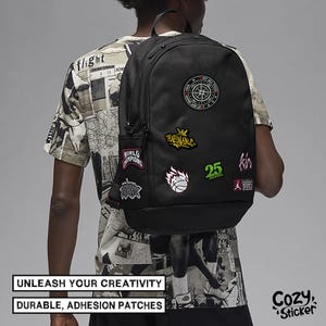May include: Black backpack adorned with colorful patches, including a compass, a crown, and a basketball. The backpack has a side pocket and is worn by a person. Text on the image reads "UNLEASH YOUR CREATIVITY" and "DURABLE, ADHESION PATCHES".