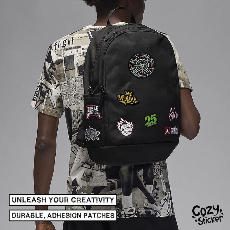 May include: Black backpack adorned with colorful patches, including a compass, a crown, and a basketball. The backpack has a side pocket and is worn by a person. Text on the image reads "UNLEASH YOUR CREATIVITY" and "DURABLE, ADHESION PATCHES".