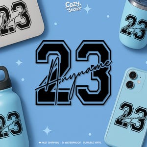 May include: Black and white number 23 design with the word "Anyname" in a script font. The design is featured on a sticker, a phone case, a tumbler, and a water bottle. The background is light blue with the text "Cozy Sticker".
