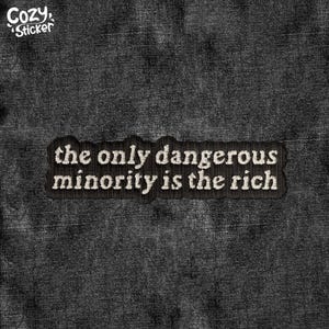 May include: A black embroidered patch with the text "the only dangerous minority is the rich" in white thread. The patch is rectangular with a black border and is set against a dark denim background. The Cozy Sticker logo is in the upper left corner.