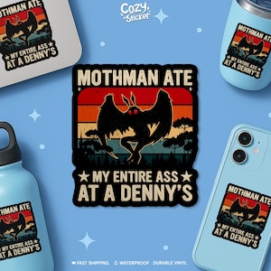 May include: A sticker featuring a black Mothman silhouette with red eyes against a sunset background. Text reads "Mothman Ate My Entire Ass At A Denny's." The design is repeated on a water bottle, a tumbler, and a phone case.