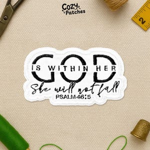 May include: A white patch with black text that reads "GOD IS WITHIN HER She will not fall PSALM 46:5". The patch has a black border and is surrounded by sewing supplies.