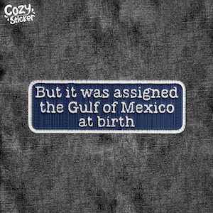 May include: A blue denim patch with white stitching reads "But it was assigned the Gulf of Mexico at birth."