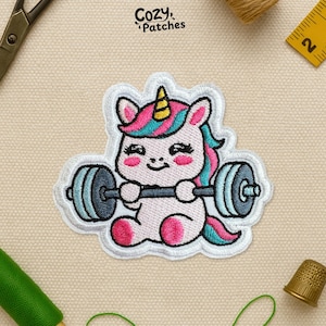 May include: A pink, blue, and yellow embroidered patch featuring a cartoon unicorn lifting a barbell. The unicorn has a yellow horn, pink ears, and blue and pink hair. The patch is outlined in white and has the text "Cozy Patches" at the top.