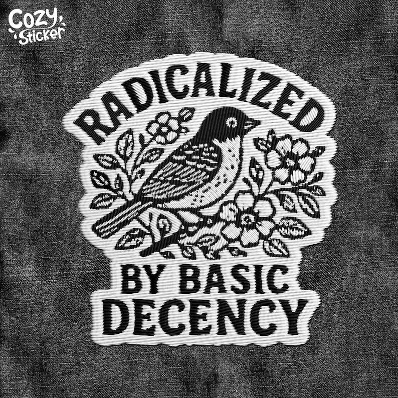 Puede incluir: Parche en blanco y negro con el texto "RADICALIZED BY BASIC DECENCY" que rodea una ilustraci&oacute;n detallada de un p&aacute;jaro posado en una rama florecida. El parche tiene un borde cosido y las palabras "Cozy Sticker" en la esquina superior izquierda.