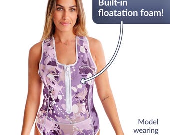 Pode incluir: Um fato de banho com padrão roxo e branco com fecho frontal e acabamento branco. O texto "Built-in floatation foam!" é exibido. A modelo está a usar o tamanho M.