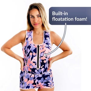 Puede incluir: Un traje de baño de estampado floral con cierre de cremallera y espuma de flotación incorporada. El traje de baño es rosa, morado y negro.