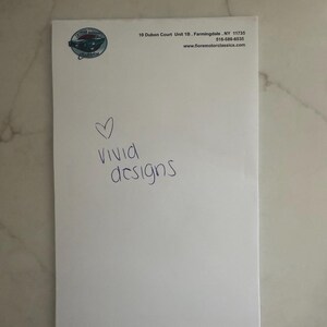 May include: A white sheet of paper with a logo and text. The logo is a circular design with a car image. The text reads "Vivid designs" in blue handwriting, with a heart symbol above the word "vivid".
