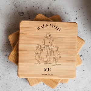 May include: Square wooden coaster with the words "WALK WITH ME" engraved at the top. Below the text is an illustration of a figure holding hands with two children. The text "MOSES 6:31" is at the bottom. The coaster is made of light-colored wood.