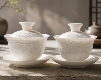 May include: Two white porcelain gaiwan tea sets, each featuring a lid with a flared knob and a matching saucer. The bowls are decorated with intricate, raised relief carvings of mythical creatures and swirling clouds across the exterior surface.