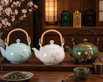 May include: Three ceramic teapots in light blue, white, and green, each with a bamboo handle and floral detailing. A small teacup and a dish of tea leaves are also present, suggesting a tea set.
