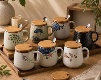 May include: A collection of seven ceramic mugs with speckled finishes, each featuring a wooden lid and a small metal spoon with a flower-shaped handle. The mugs display various painted designs including fish, flowers, and birds, arranged on a wooden tray.