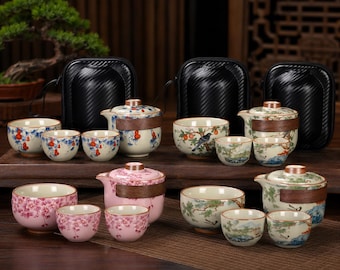 May include: Four ceramic tea sets, each featuring a teapot with a wooden band and three matching cups. The sets display various painted designs including red gourds, birds with fruit, pink cherry blossoms, and green landscapes, paired with black cases.