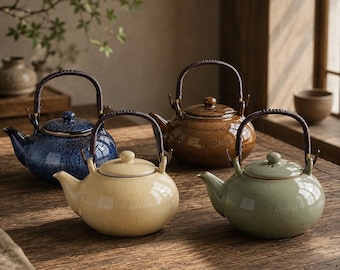 May include: Four ceramic teapots with rounded bodies and lids, each featuring a dark, wrapped arched handle. The teapots are finished in glossy glazes of deep blue, warm brown, cream, and sage green, all displaying a subtle crackle texture.