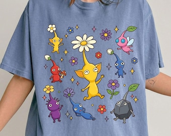 May include: Blue t-shirt featuring a colorful graphic of cartoon creatures with flower-like heads and various colors. The shirt has the text "Blue Jean" at the bottom.