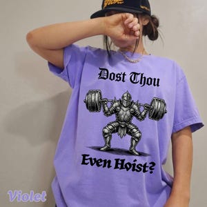 Op de afbeelding: Violetkleurig T-shirt met een afbeelding van een ridder die een halter optilt. De tekst "Dost Thou Even Hoist?" staat boven en onder de illustratie in gotisch lettertype. Het shirt heeft een comfortabele pasvorm.