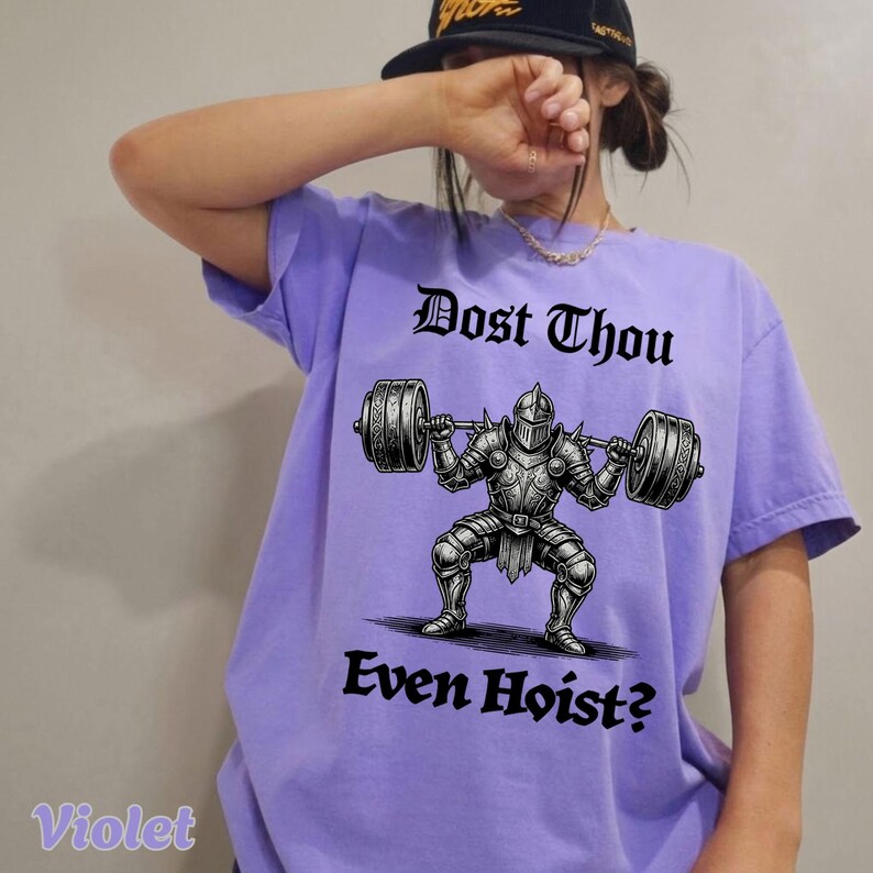 Op de afbeelding: Violetkleurig T-shirt met een afbeelding van een ridder die een halter optilt. De tekst "Dost Thou Even Hoist?" staat boven en onder de illustratie in gotisch lettertype. Het shirt heeft een comfortabele pasvorm.