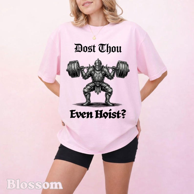 Op de afbeelding: Lichtroze t-shirt met de tekst "Dost Thou Even Hoist?" boven en onder een afbeelding van een ridder die gewichten heft. De ridder draagt een harnas en tilt een halterstang op.