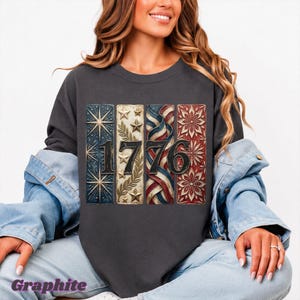 May include: Dark gray sweatshirt with a patriotic design featuring the number "1776" in a vertical, rectangular format. The design incorporates stars, stripes, and floral patterns in red, white, and blue.