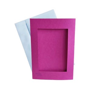 May include: A blank card with a magenta frame and a white envelope. The card has a cut-out window for a photo and the text "Recycled Paper" in the bottom left corner.