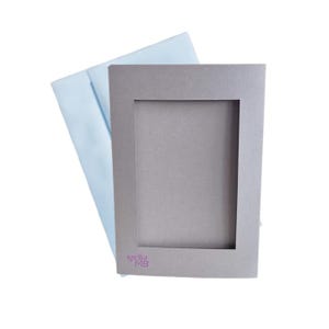 May include: A gray card with a rectangular window cut out. The card has a pink logo that says "kocilia MB".