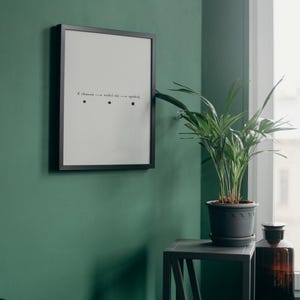 May include: A black framed print with the text "Z. chanon --- rodel ale --- spokey" and three black dots on a green wall. A potted plant with green leaves sits on a black metal stand.