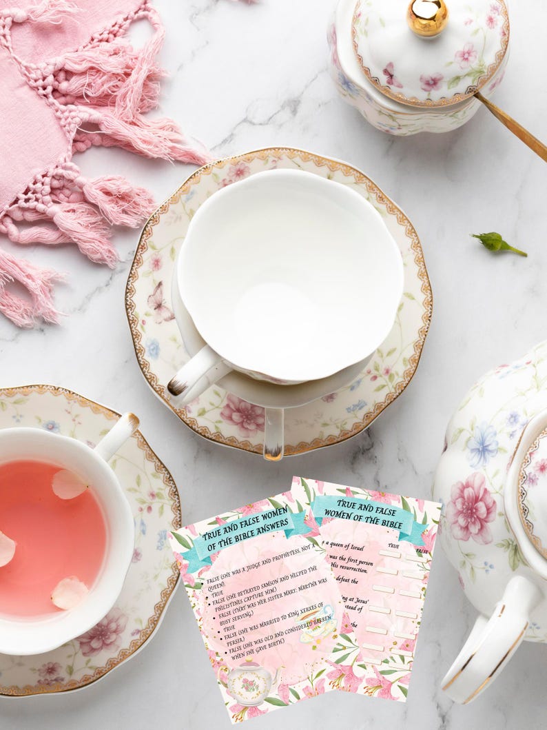 May include: An overhead view of a floral tea set, comprising a teapot, teacups, and saucers. One teacup holds pink tea. Two cards with the text "True and False Women of the Bible Answers" are visible. A pink scarf is in the background.