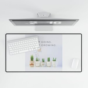 Peut inclure: Un tapis de bureau blanc avec une bordure noire, comportant une citation "Keep going. Keep growing." et une rangée de cinq succulentes en pot. Un clavier blanc et une souris d'ordinateur blanche sont également sur le tapis.