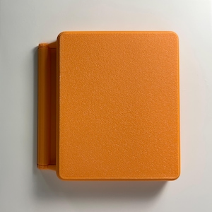 May include: A small, orange, rectangular box with a textured surface. The box has a hinge on one side and can be opened.