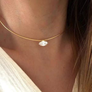 May include: A delicate gold necklace featuring a marquise-cut diamond pendant. The diamond is clear and sparkling, suspended from a thin, gold chain. The necklace is worn around the neck, showcasing the elegant design.
