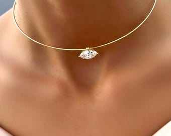 May include: A gold choker necklace featuring a marquise-cut diamond pendant. The pendant is a clear, sparkling gemstone. The necklace is worn around the neck.