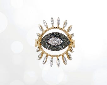 May include: A gold ring with a black and white diamond eye design. The eye is surrounded by a circle of smaller diamonds.