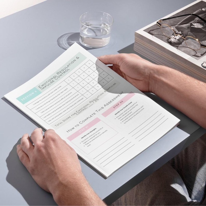 以下が含まれることがあります： 「感情調節と衝動制御」と題された印刷された評価フォームを人が持っています。フォームには採点用のグリッドと指示があります。背景には水を入れたグラスと書類の山があります。
