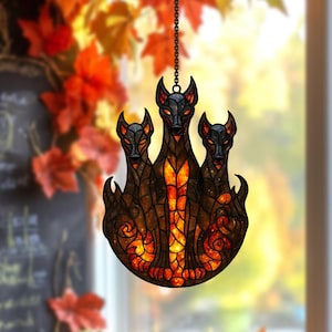 May include: A stained glass window hanging featuring three black dogs with red eyes and a fiery orange and yellow center. The decorative piece is suspended by a chain and has a decorative flame-like base.