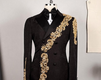 May include: A black double-breasted tuxedo jacket with gold floral embroidery on the lapel and sleeves. The jacket features a black satin lapel, a white dress shirt, and a black bow tie. The jacket is displayed on a mannequin.