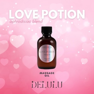 May include: A brown glass bottle with a black label that reads "DELULU LOVE POTION massage oil ylang ylang jasmine patchouli". The bottle is on a pink background with hearts.