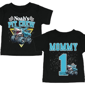 以下が含まれることがあります： モンスター・トラックのデザインが施された黒いベビーTシャツ。1枚は「Noah's PIT CREW」とサメをテーマにしたトラックが描かれています。もう1枚は「MOMMY」と「1」とモンスター・トラックが描かれています。どちらのシャツにもチェッカーフラッグが付いています。