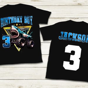 May include: Black t-shirts with a shark-themed design. One shirt features "BIRTHDAY BOY" and a shark monster truck with the number "3". The other shirt has the name "JACKSON" and the number "3".
