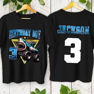 May include: Black t-shirts with a shark-themed design. The front features the text "BIRTHDAY BOY" and a shark monster truck with the number "3". The back displays the name "JACKSON" and the number "3".