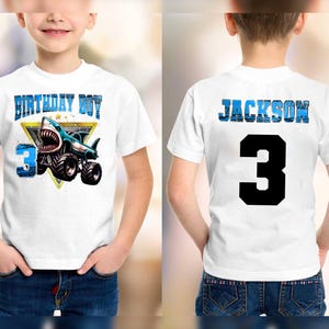 May include: White t-shirt with a shark monster truck graphic. The front of the shirt says "BIRTHDAY BOY" and "3". The back of the shirt says "JACKSON" and the number "3".