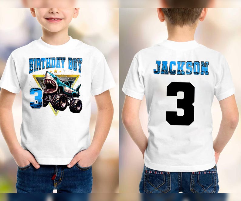 May include: White t-shirt with a shark monster truck graphic. The front of the shirt says "BIRTHDAY BOY" and "3". The back of the shirt says "JACKSON" and the number "3".