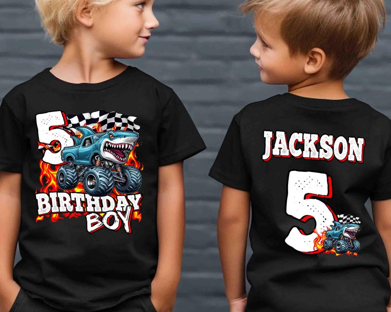 Puede incluir: Camiseta negra con un dise&ntilde;o de cami&oacute;n monstruo con una cabeza de tibur&oacute;n, llamas y el texto "5 BIRTHAY BOY". La parte trasera de la camiseta tiene el nombre "JACKSON" y el n&uacute;mero "5".