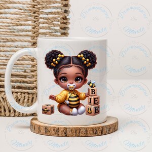 May include: White ceramic mug featuring a cartoon illustration of a baby girl dressed as a bee. The baby is holding wooden blocks that spell out "BEE". The mug sits on a wooden coaster.