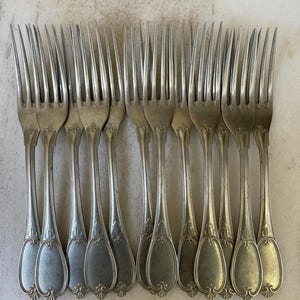 May include: A set of antique silver forks. Each fork has a long, slender handle with an ornate, oval design at the base. The tines are long and pointed. The forks are arranged in a neat, parallel row.