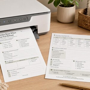 May include: Two white printed paper sheets featuring a Sunday Reset When You Feel Behind planner layout with checkboxes, lined sections, and structured task lists, resting on a wooden surface next to a printer, a coffee mug, and a pen.