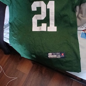 Puede incluir: Camiseta de fútbol verde y blanca con el número 21 en la parte delantera. La camiseta tiene un logotipo de la NFL blanco y un logotipo de "Jets" blanco en la parte delantera.